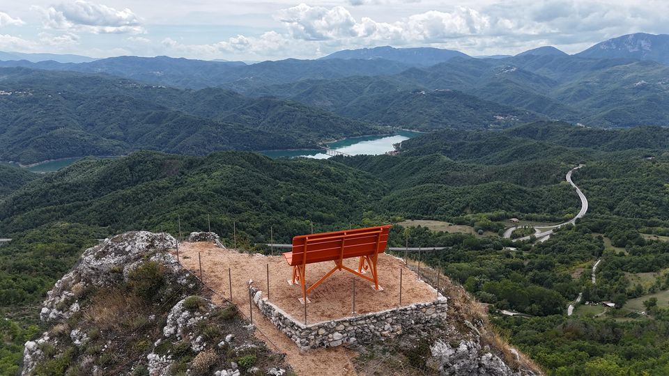 Una Big Bench arancione affacciata su una valle con lago e montagne.