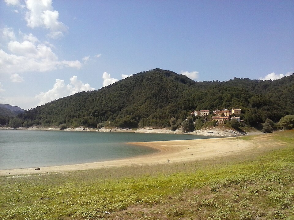 Una riva scoperta del Lago del Salto con case ai piedi di una collina boscosa.